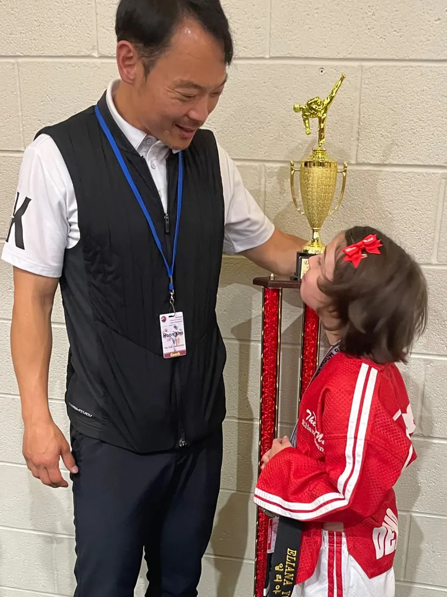 Instructor congratulating a young competitor beside the team trophy