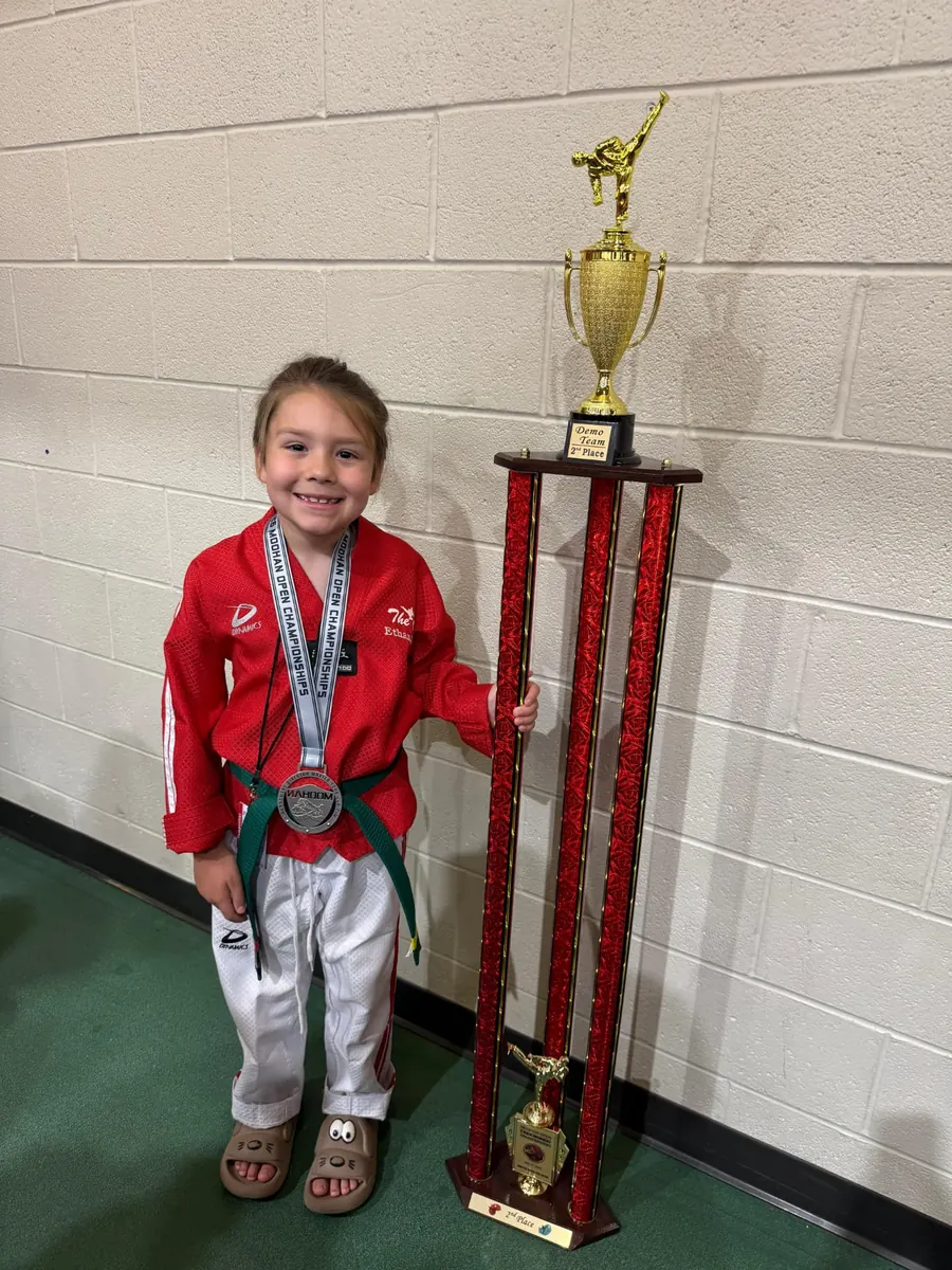 Young demo team competitor posing beside the team trophy