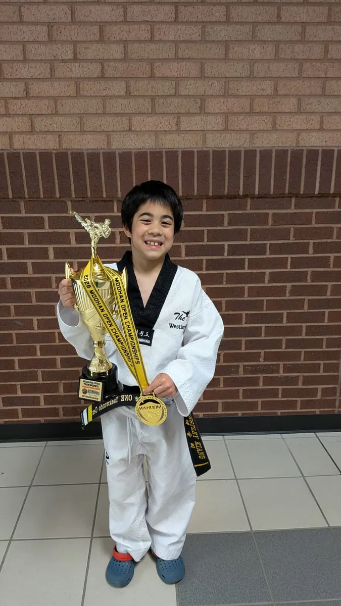 Young black belt smiling with his trophy and gold medal